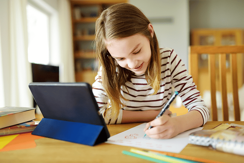 Young girl sitting at table with tablet and pencil